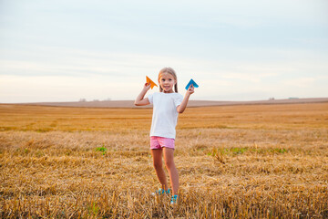 Cute child girl running and playing toy paper airplane in the field in summer day