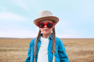 funny little girl with pigtails in sunglasses and straw hat outdoor in summer day. Summertime