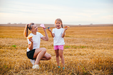 Happy mother and daughter are playing with paper airplanes outdoor