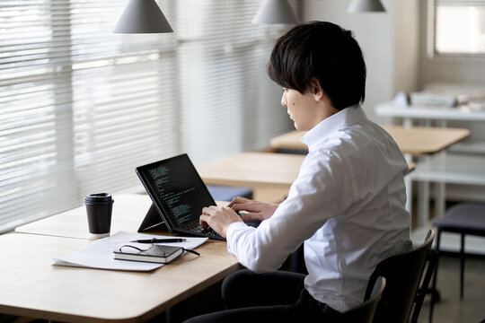 ノートパソコンでコードを書くアジア人プログラマー