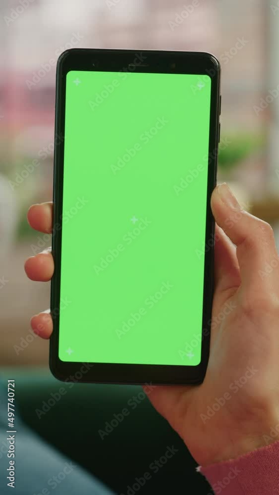 Fototapete vertical screen: feminine hand scrolling feed on smartphone with green screen mock up display. femal
