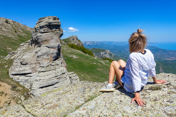 Naklejka premium A girl on the background of a view of the Black Sea and the stone conglomerates of the Demerdzhi ridge. May.
