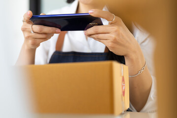Female small business owner using mobile app on smartphone scanning barcode checking parcel box. Woman running a small online business using mobile phone taking pictures of parcels sent to customers.