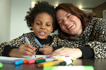 Caucasian mother and an African-American daughter are drawing together at home.Diverse people.Time...