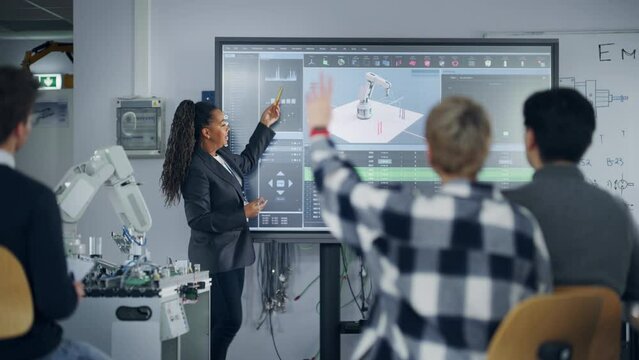 Smart Black Teacher Explaining Near Big Screen and Robotic Hand to Students During Lesson. Team of Young Engineers Listening Information at University. Robot vision and Programming Language Concept
