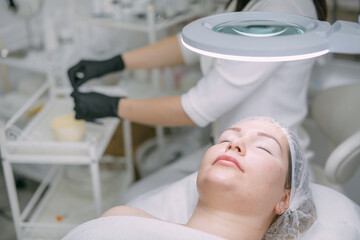 Young woman on a cosmetology facial skin care procedure in a beauty salon. Cosmetologist and dermatologist performs a facial procedure
