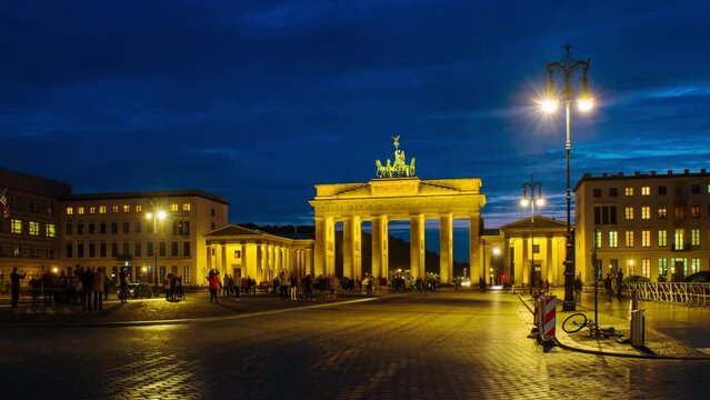 Berlin, Germany. Illuminated Brandenburg Gate at night in Berlin, Germany. Dark blue sky, blurred people. Time-lapse, zoom in