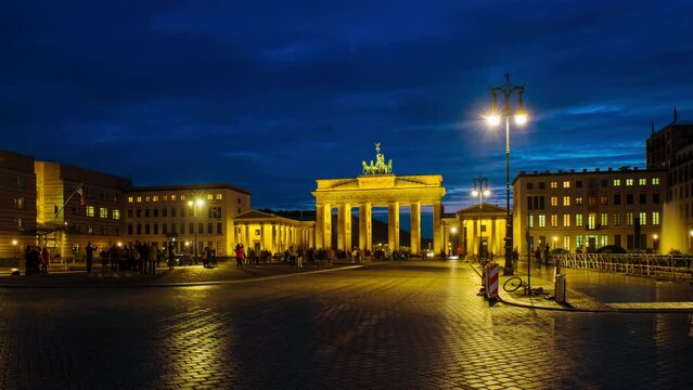 Berlin, Germany. Illuminated Brandenburg Gate at night in Berlin, Germany. Dark blue sky, blurred people. Time-lapse
