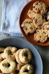 Plate of chocolate chip cookies and bowl of sugar cookies on wooden table. Flat lay.
