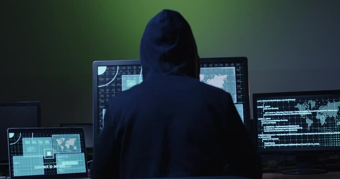 Hacker hacks data, sits in front of three monitors with windows and computer code in the dark. Cyber protection against hacker attacks.