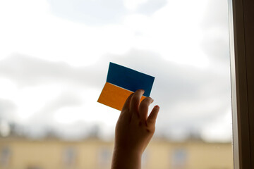 War in Ukraine. The child looks out the window with the flag of Ukraine. Baby with heart of flag of...