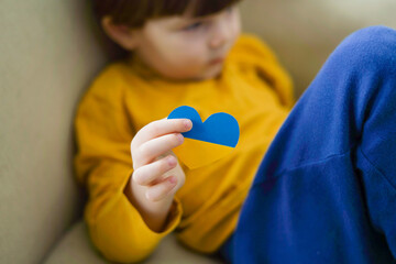 War in Ukraine. The child looks out the window with the flag of Ukraine. Baby with heart of flag of...