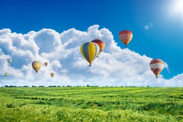 Multicolored hot air balloons fly in blue sky with white clouds over green field