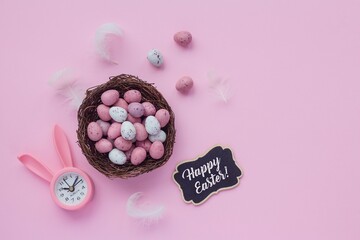 Small chocolate Easter eggs in a nest on a pink background. Flat lay shot. Happy Easter card