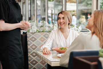Two Happy and Cheerful Women Having Lunch Time, Making Order to Female Waiter in the Restaurant