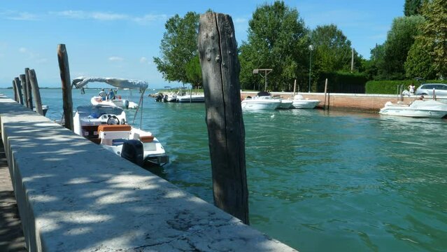 fantastic jetty on a blue green sea  in Italy,  near Venice (canale portosecco), with little boats looked on the poles and one passing by all in all a a beautiful sunny summer day with blue sky