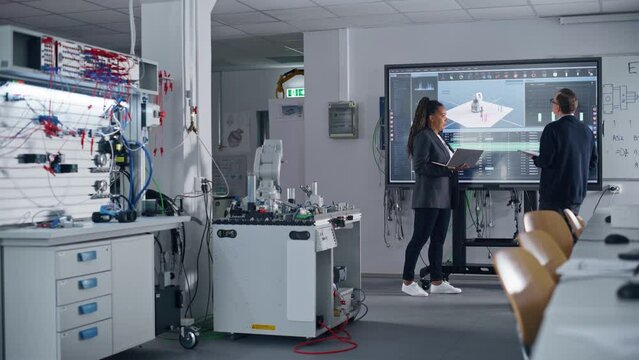 Two Male and Female Diverse Teachers Standing Near Big Screen and Developing Program for Motion of Robotic Arm. Science and Innovative Technologies Concept