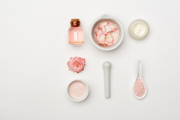 Fototapeta na wymiar top view of flower near pestle and mortar with petals, sea salt, cream and bottle with rose water on white.