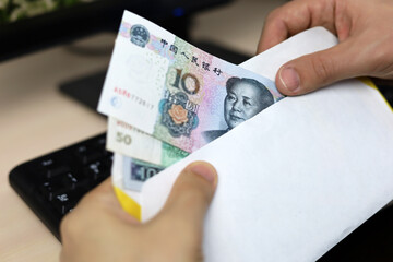 Envelope with Chinese yuan in male hands. Man pulls money out of an envelope on PC keyboard...