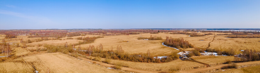 Aerial view of fields with copse, dry yellow grass, a stream, remnants of snow in early spring. Nature background.