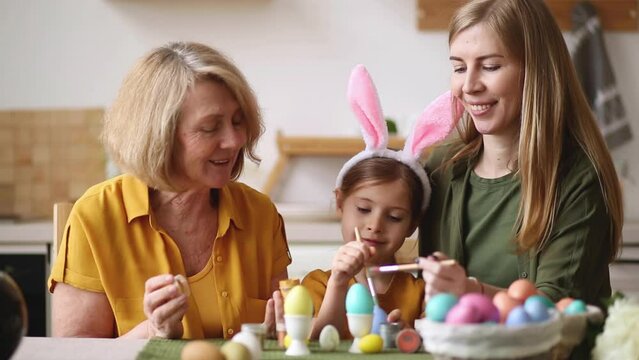 Happy easter family elderly grandmother and young woman mother blonde with little daughter with rabbit ears are preparing for the holiday to paint eggs