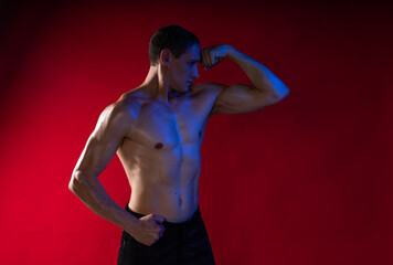 bare-chested man in colored light. showing muscles posing with dumbbells and smoke. standing or on the floor. red background. Studio