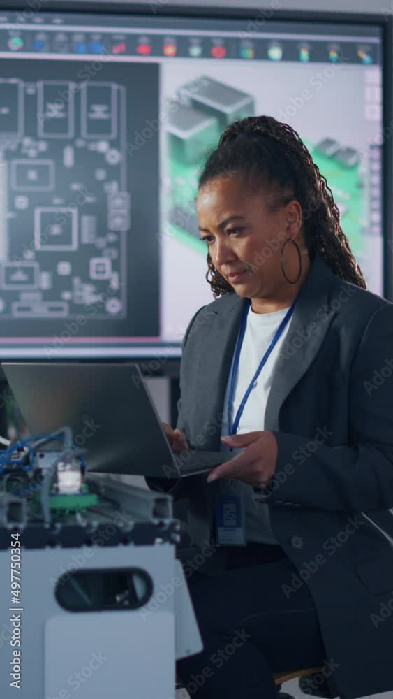 Aufkleber Black Developer Typing at Laptop while Programming Robotic Arm at Laboratory. Woman Coding with Concentrated Face. Computer Language and Programming Concept. Vertical Video