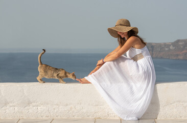 Young beautiful pretty woman in white dress with long hair sitting on white wall in Santorini greek...