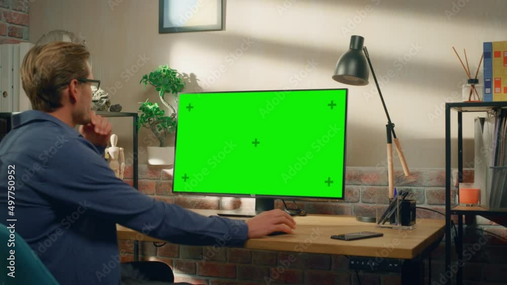Poster young handsome man sitting down to work from home on desktop computer with green screen mock up disp