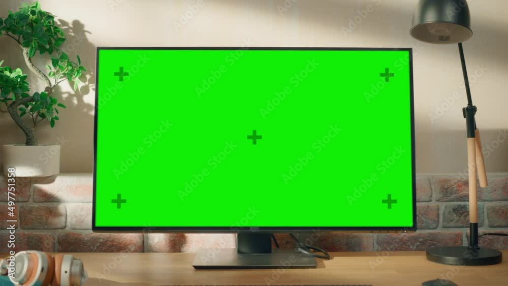Poster Desktop Computer Monitor Standing on a Desk with a Green Screen Chromakey Mock Up Display. Cozy Empty Loft Apartment with a Lamp, Notebooks and Smartphone on the Table. Zoom Out Shot.