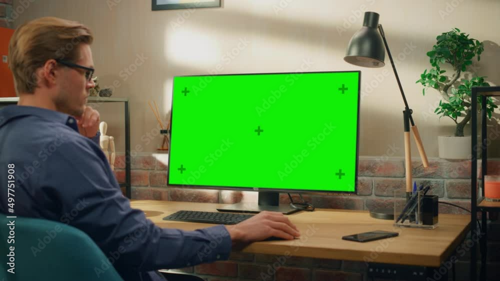 Poster Young Handsome Man Working from Home on Desktop Computer with Green Screen Mock Up Display. Creative Male Checking Social Media, Browsing Internet. Living Room in Bright Loft Apartment. Arc Shot.