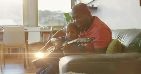 Animation of light spots over happy african american father playing guitar with son - Powered by Adobe