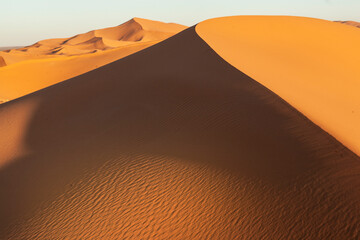 Paesaggio desertico con dune di sabbia alte e sfondo cielo blu