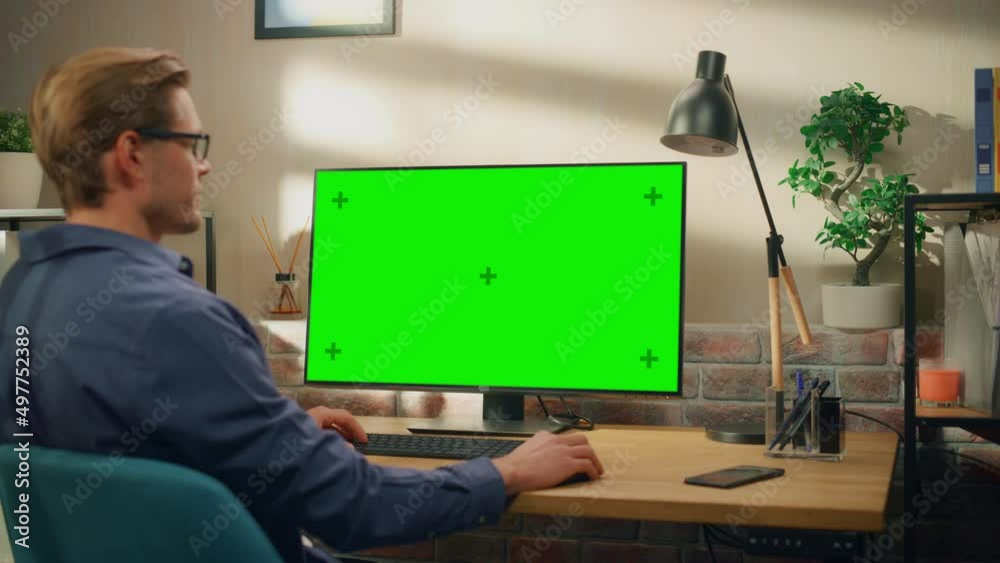 Poster Young Handsome Man Working from Home on Desktop Computer with Green Screen Mock Up Display. Creative Male Checking Social Media, Browsing Internet. Living Room in Bright Loft Apartment. Static Shot.