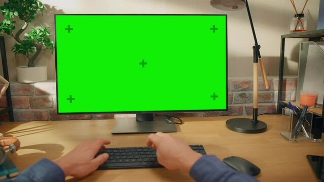 POV First Person View of a Man Working on Desktop Computer with Green Screen Mock Up Display. Male Sitting at a Desk, Typing on Keyboard and Using Mouse at Home in Stylish Living Room.