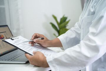 Doctor write health medical note in clipboard with laptop in hospital.