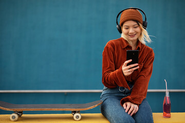 Portrait of fashion Asian woman with skateboard. Urban blonde woman listening the music while enjoy outside