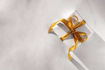Gift box wrapped in white paper with a golden bow on festive light background. Copyspace for your...