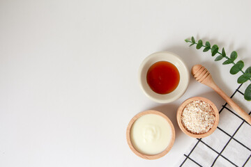 Natural ingredients for homemade face mask, top view of yoghurt, oat and honey on white background, beauty skincare product concept, flat lay