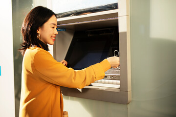 Fototapeta na wymiar Happy smiling young woman withdrawing money from credit card. Young woman typing pin code on keypad of ATM machine.