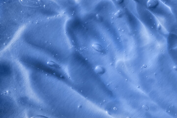 Texture of transparent blue gel with air bubbles and waves on orange background. Concept of skin moisturizing, body care and prevention of covid19. Liquid beauty product closeup. Backdrop, flat lay
