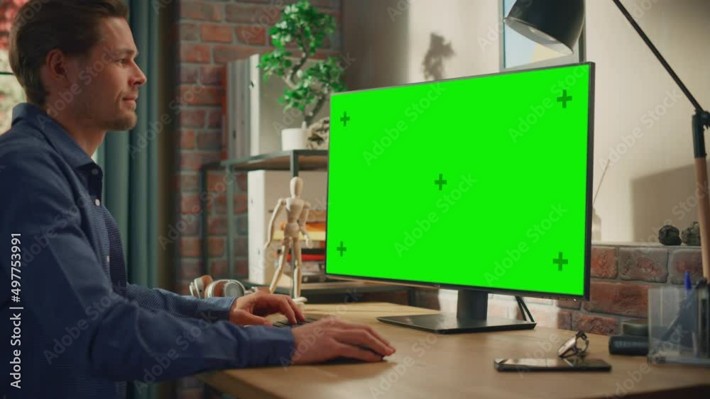 Poster young handsome man working from home on desktop computer with green screen mock up display. male che
