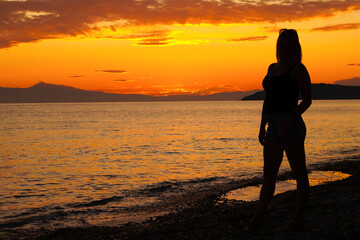 Fototapeta premium Sunset. Silhouette of a woman on the shore of the Aegean Sea. Greece.