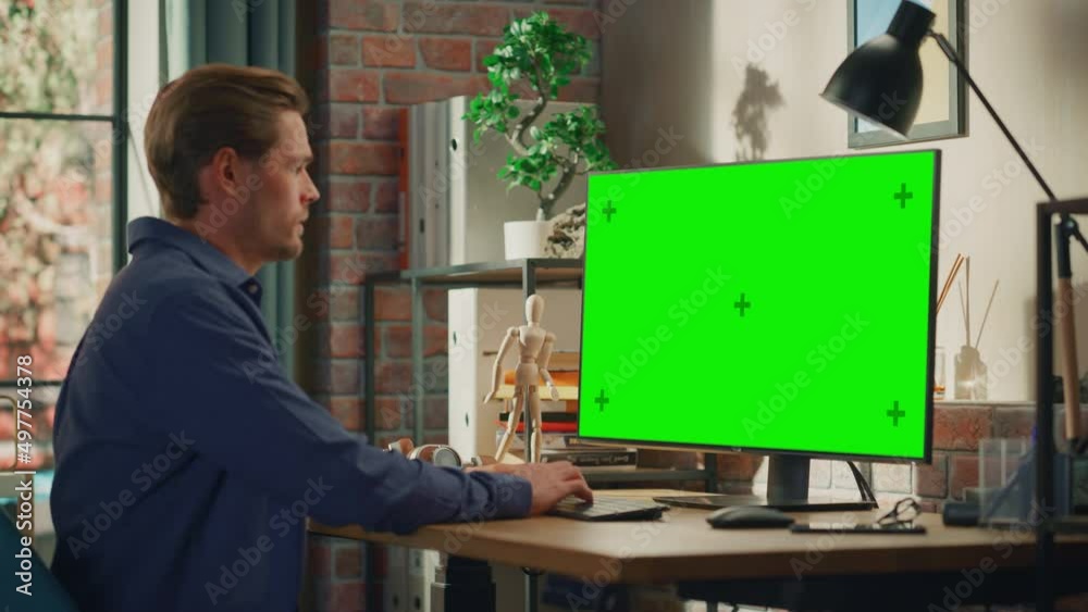 Poster young handsome man sitting down to work from home on desktop computer with green screen mock up disp