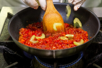 The cook cooks tomato sauce with celery in a frying pan