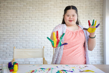 down syndrome teenage girl showing painted hands, drawing a picture on paper