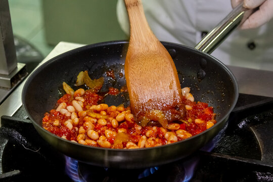 The cook cooks white beans with tomato sauce in a frying pan