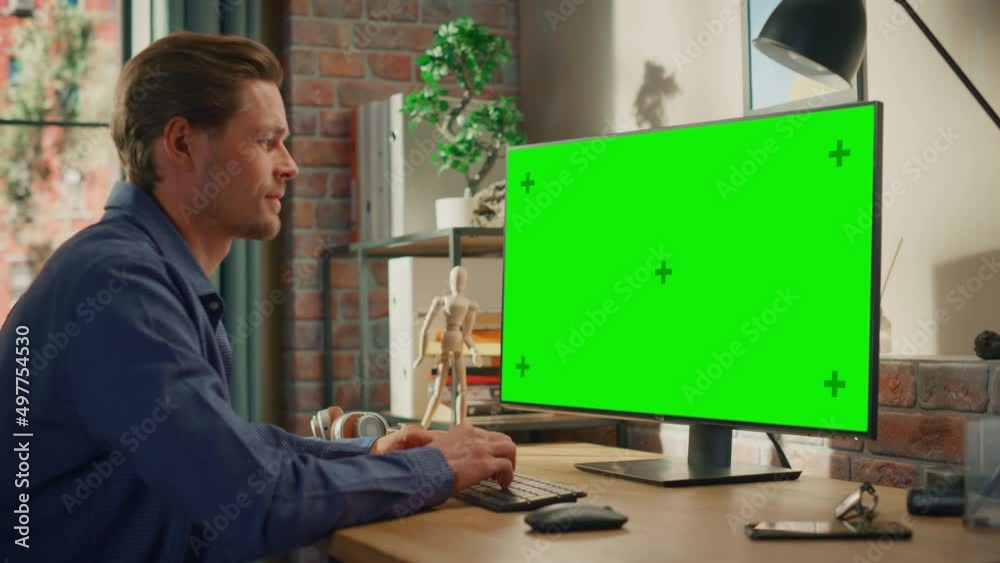 Poster young handsome man working from home on desktop computer with green screen mock up display. male che