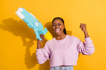 Portrait of delighted carefree person raise fist scream yeah hold water pistol isolated on yellow color background