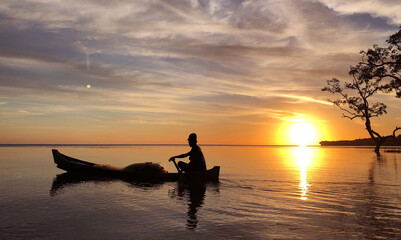 Naklejka na ściany i meble Fisherman sailing in small boat at sunset